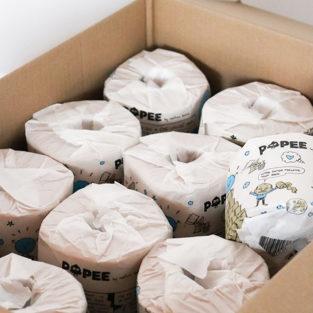 Carton contenant plusieurs rouleaux Popee x Mathieu Sapin avec emballage papier recyclé illustré.