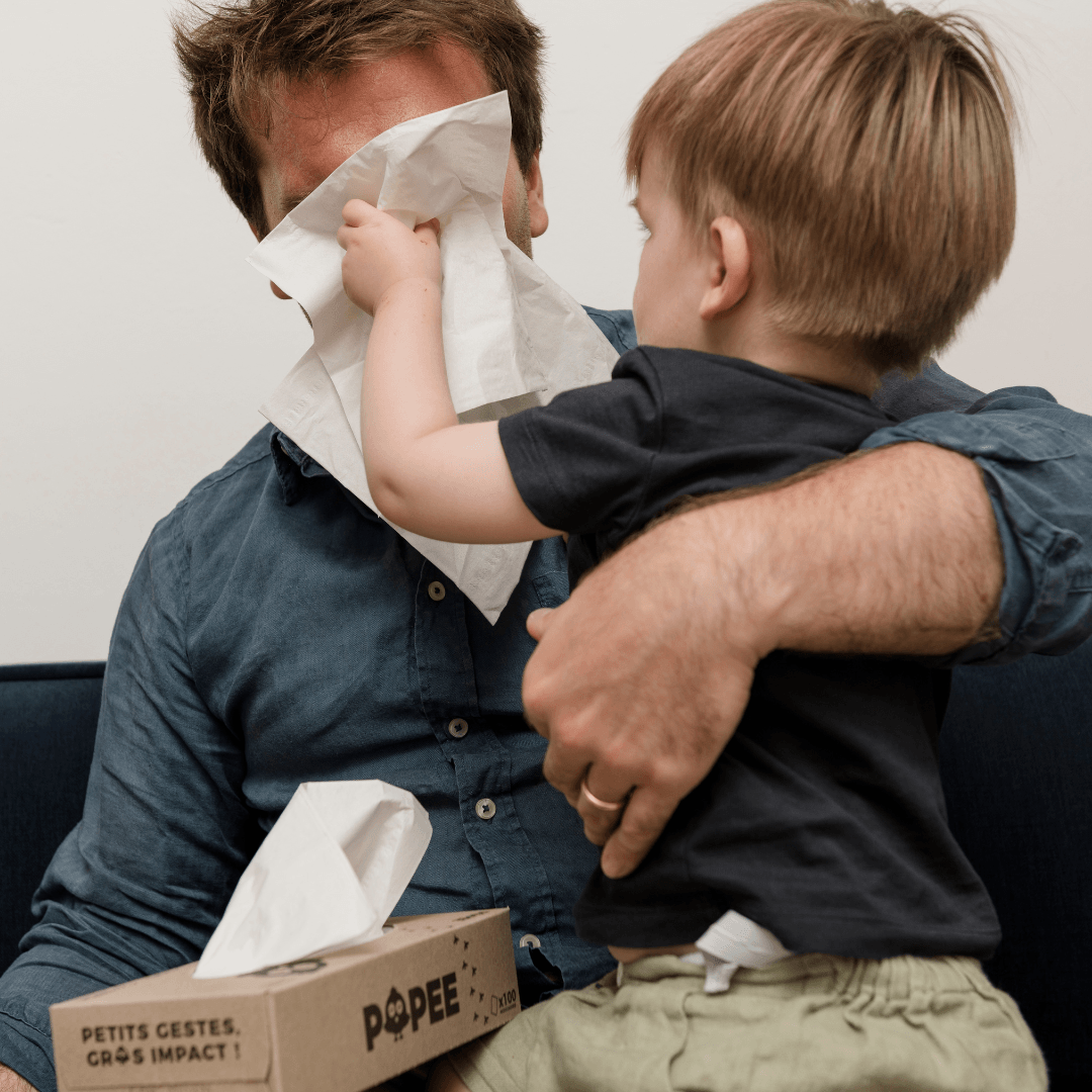 Un enfant essuie le visage de son père avec un mouchoir Popee, douceur et complicité.
