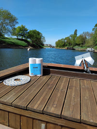 Pack de papier toilette Popee posé sur un bateau en bois, au bord d'une rivière.