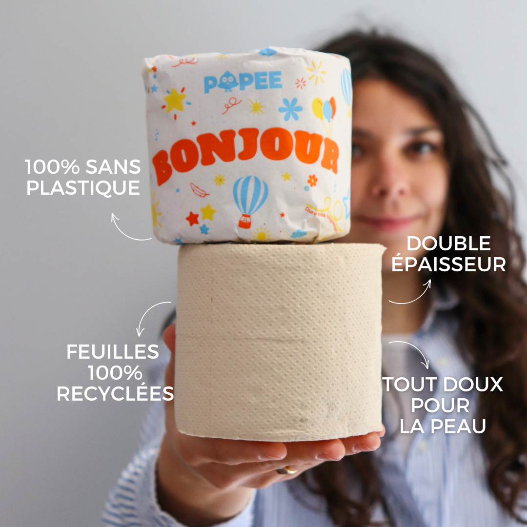 Une femme présente un rouleau Popee ‘BONJOUR’ et un rouleau nu pour comparer l’emballage 100 % sans plastique et les atouts produit.