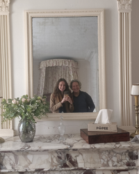 Deux femmes souriantes prennent un selfie dans un miroir ancien, au-dessus d'une cheminée en marbre où trône une boîte de mouchoirs Popee, entourée d'un bouquet de fleurs et d'objets décoratifs.