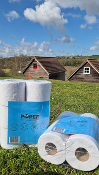 Packs de rouleaux de papier toilette Popee posés dans l'herbe devant des chalets en bois.