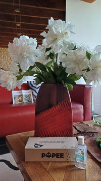 Boîte de mouchoirs Popee posée sur une table basse en bois, à côté d'un vase de pivoines blanches et d'un gel hydroalcoolique, dans un salon avec canapé en cuir rouge.