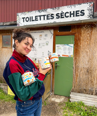 Papier toilette Popee aux motifs colorés, devant des toilettes sèches en bois avec une pancarte 