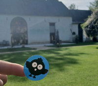 Autocollant Popee tenu devant une grange en pierre à la campagne.
