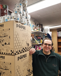Cartons Popee illustrés en bande dessinée par Mathieu Sapin, empilés dans une librairie, avec des rouleaux de papier toilette Popee disposés au sommet