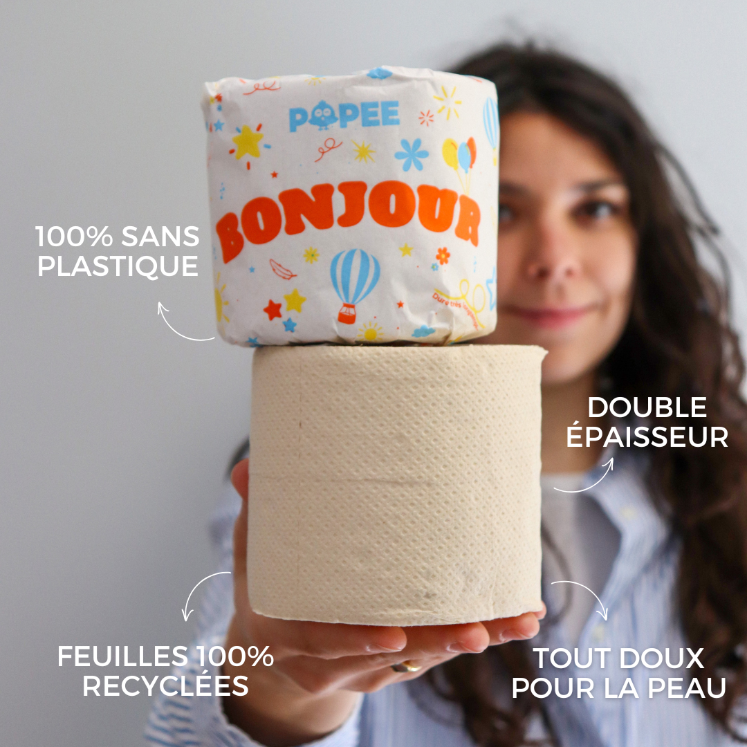 Une femme présente un rouleau Popee ‘BONJOUR’ et un rouleau nu pour comparer l’emballage 100 % sans plastique et les atouts produit.