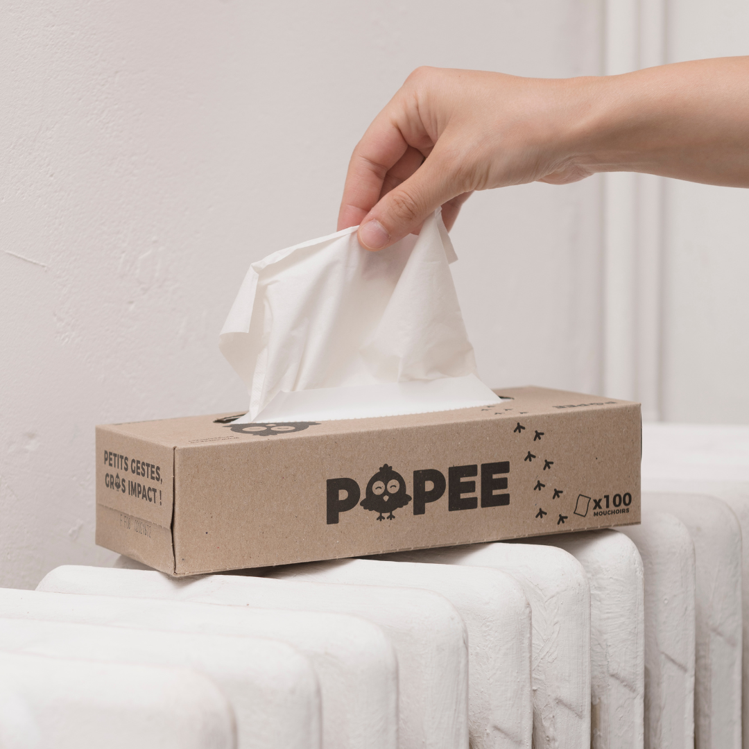 Main tirant un mouchoir en papier recyclé Popee posé sur un radiateur blanc.