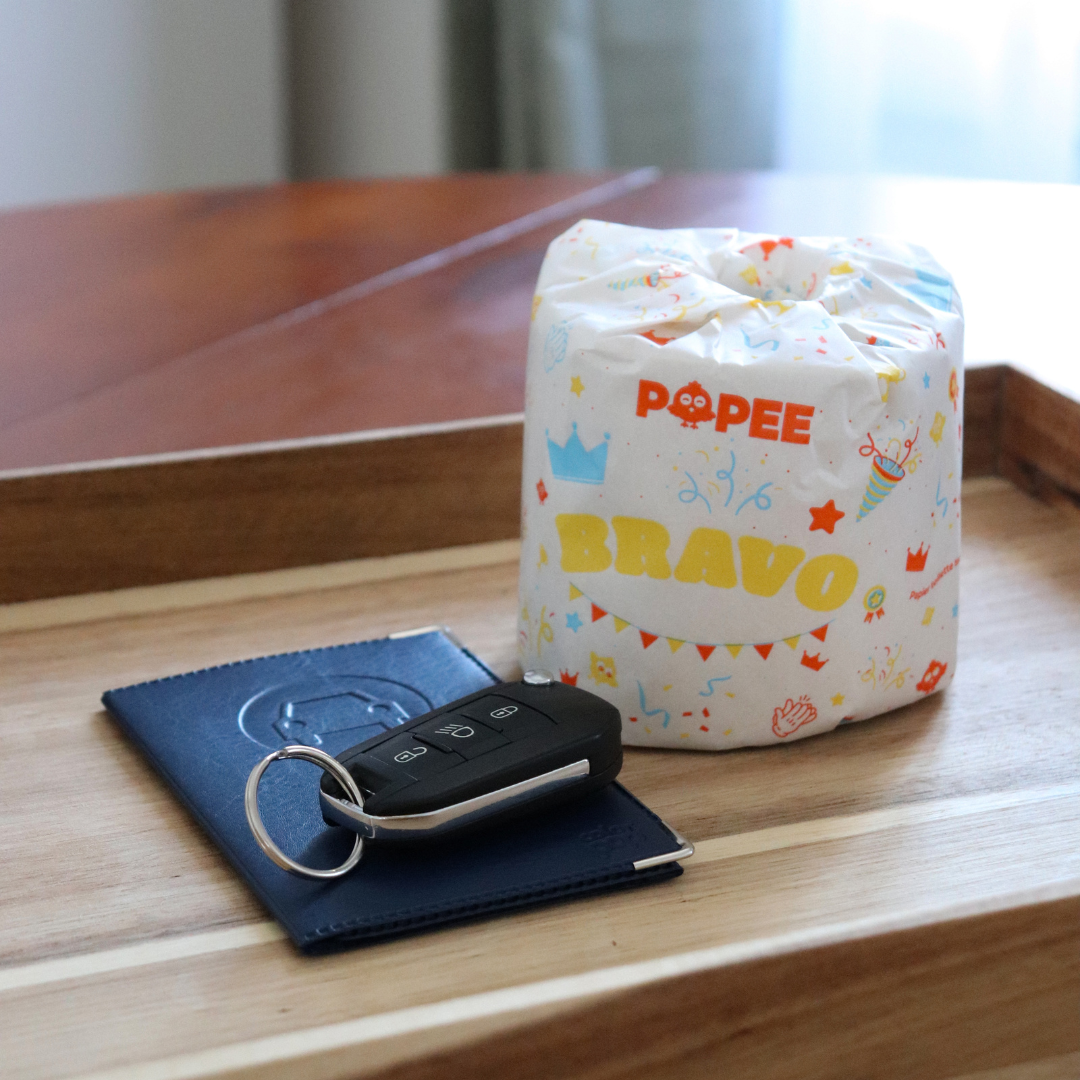 Rouleau Popee ‘BRAVO’ posé à côté d’une carte grise et de clés, clin d’œil à un cadeau ou une surprise humoristique.