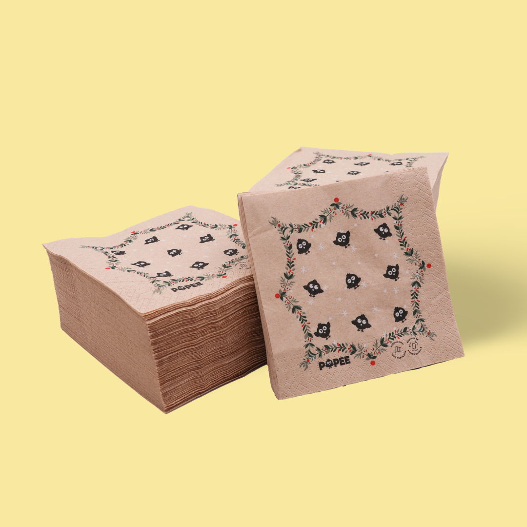Serviettes en papier recyclé POPEE à motif de Noël, double épaisseur, présentées en lot sur fond jaune.